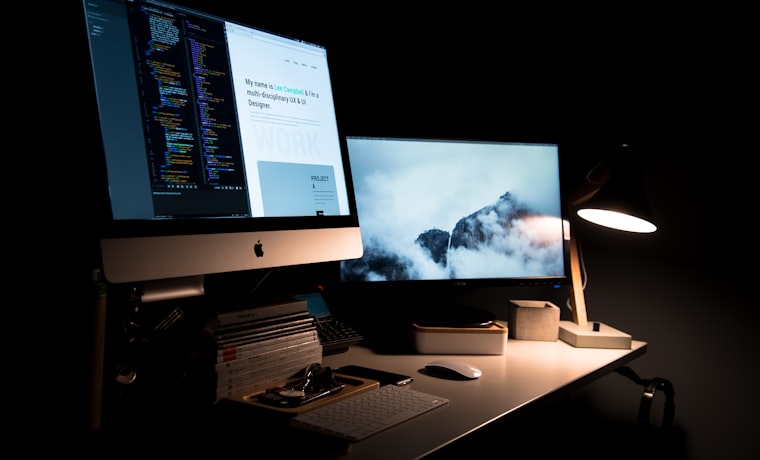 A designer's desk with code and a website on screen